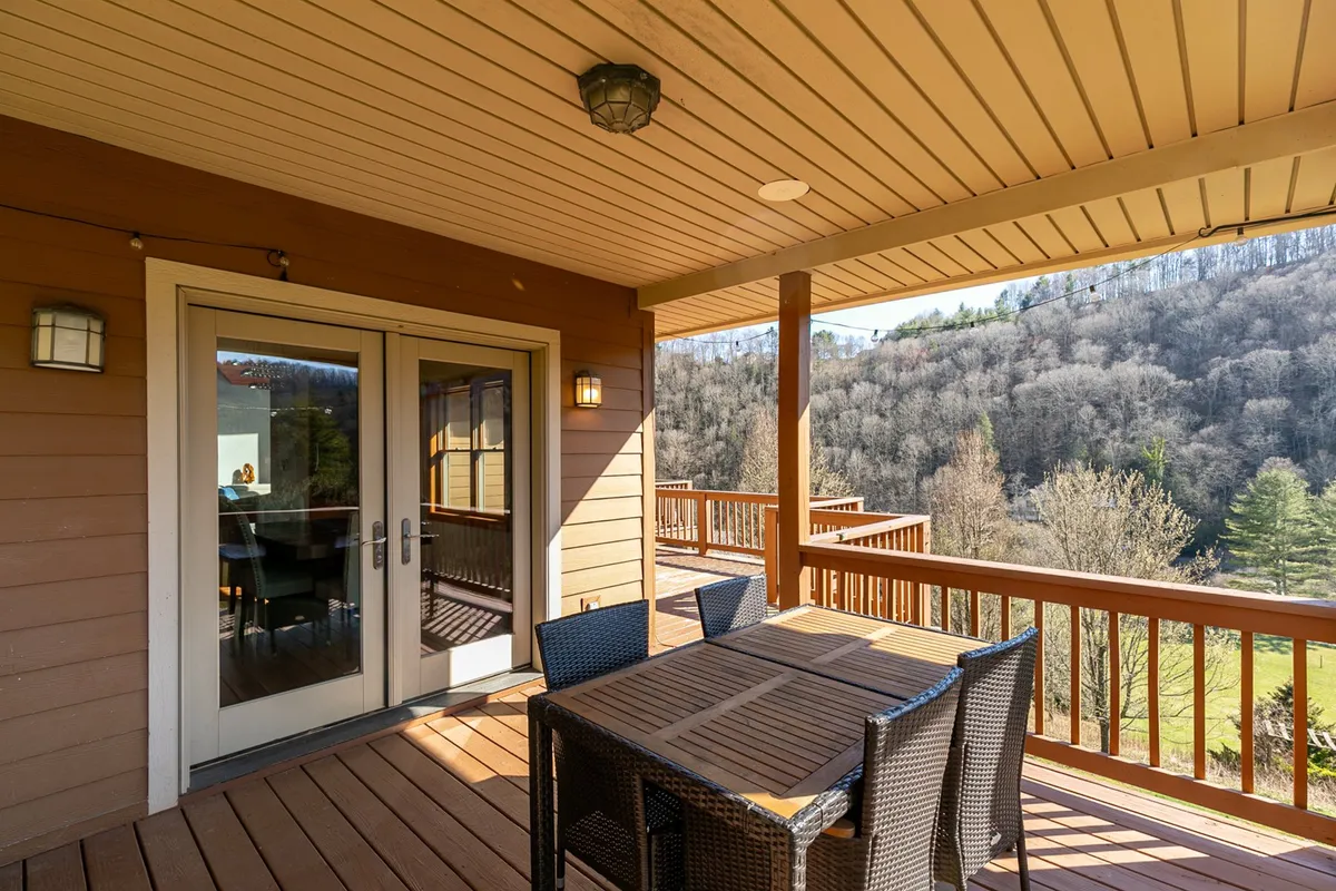 This photo showcases a spacious wooden deck equipped with an outdoor dining table and sweeping views of the surrounding mountains. The table is set for dining al fresco, making it clear this is an ideal spot for meals, gatherings, or simply unwinding in the mountain air. The wide deck and open railings maximize the sense of space and connection to nature.