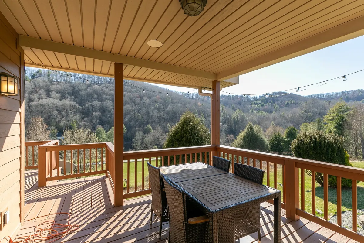 A beautifully arranged outdoor dining table sits beneath string lights, surrounded by greenery and scenic landscape views, suggesting an ideal space for group dining, morning coffee, or celebratory dinners.