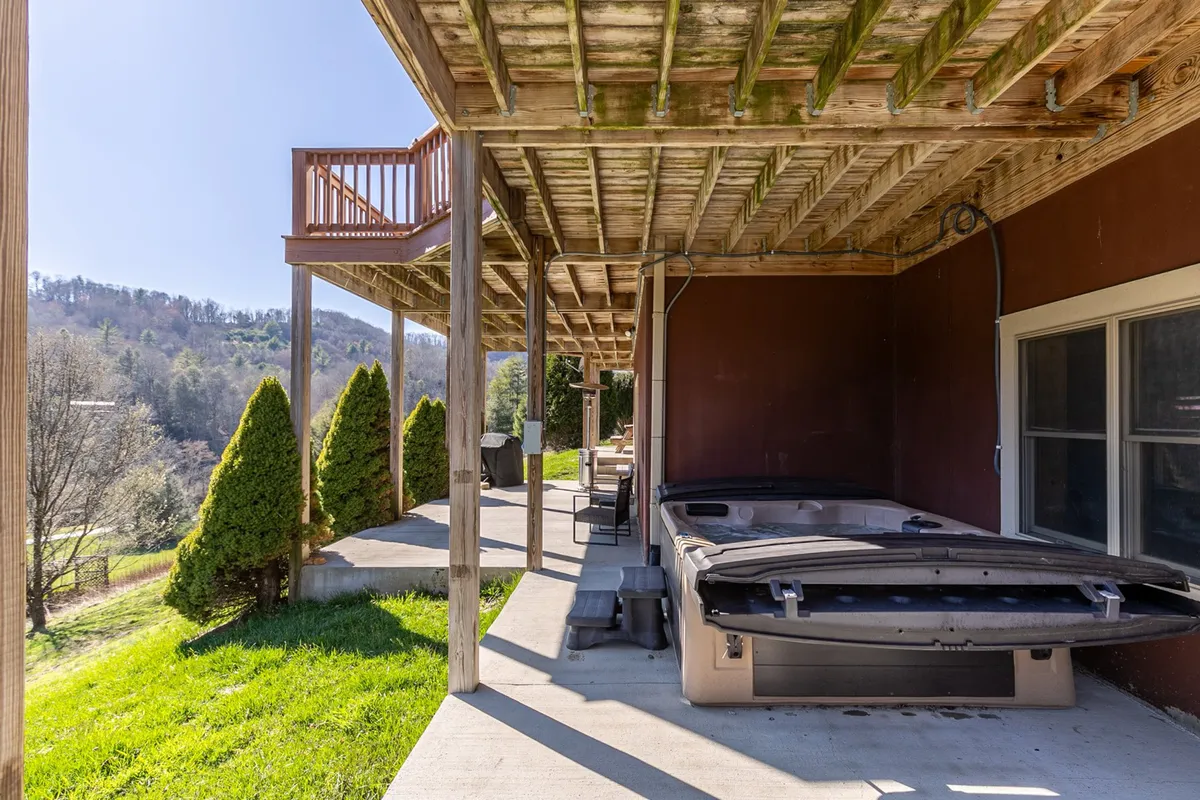 This image features a tranquil outdoor hot tub on a spacious wooden deck, surrounded by manicured shrubs and offering an expansive view of rolling hills and a glowing sunset.