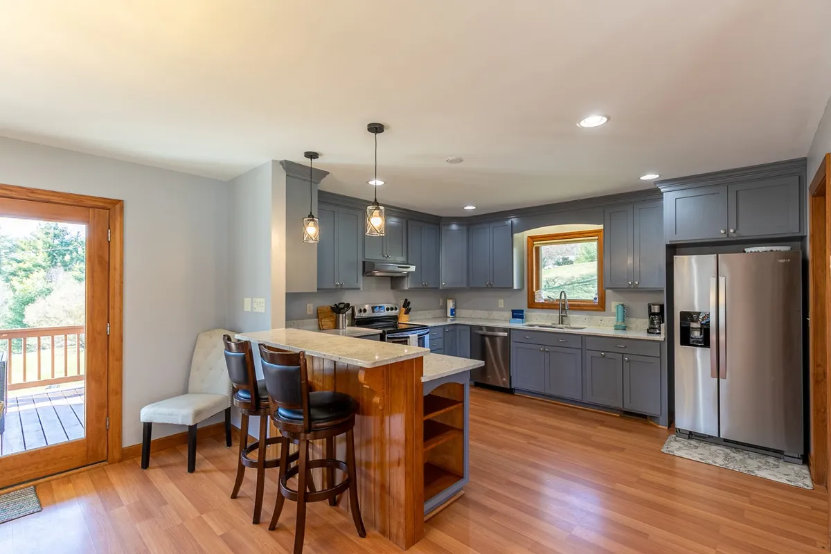 A bright kitchen featuring a large island with bar stools, stainless steel appliances, and a large window offering scenic views. The space is ideal for cooking, entertaining, and connecting with guests, and emphasizes the modern, fully stocked chef's kitchen described in the section.