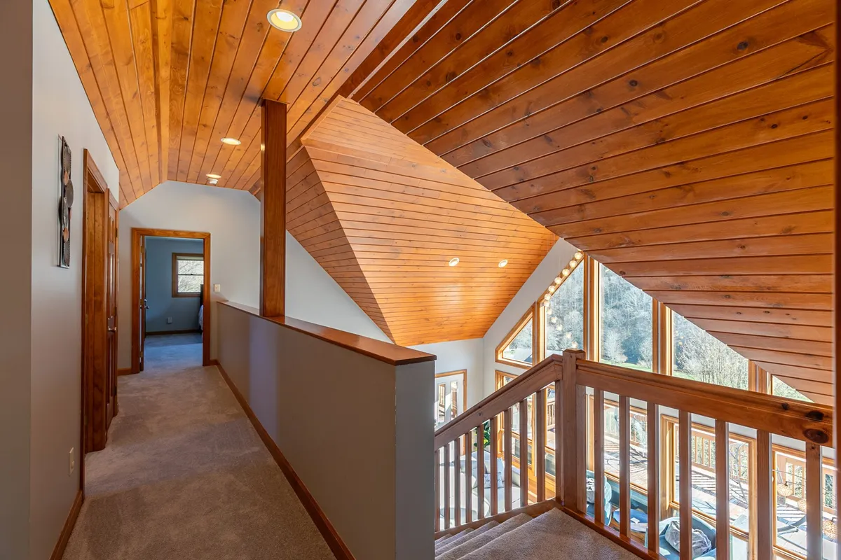 A hallway with a striking wooden ceiling, broad stair railing, and large windows that showcase the changing landscape beyond. The space feels open and inviting, ideal for welcoming guests or gathering for special occasions.