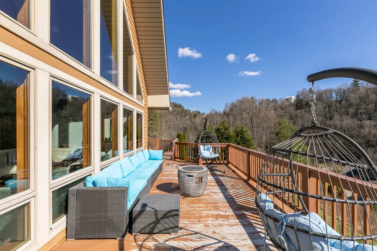 A wide view of the home's exterior showcases large windows, multiple hanging chairs, and a comfortable outdoor seating area, all framed by the natural beauty of the surrounding landscape. The warm light suggests a cozy evening setting.