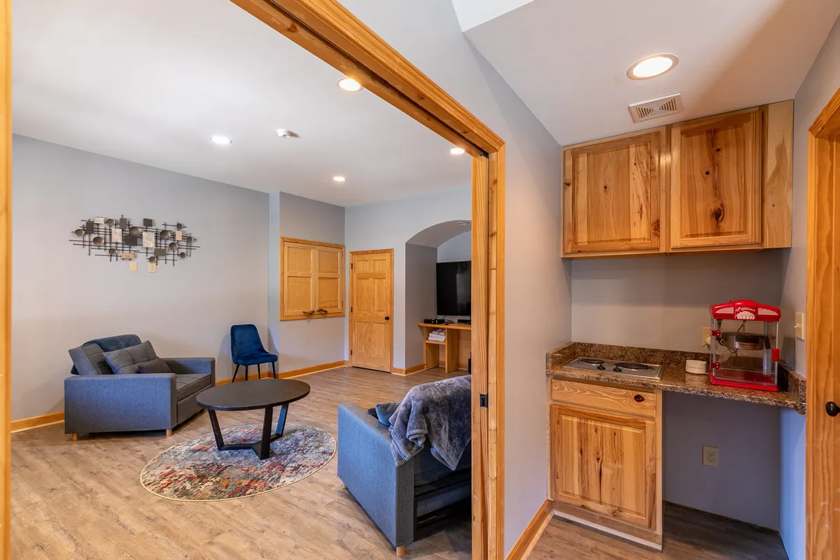 A lower-level living space featuring a cozy seating area, a kitchenette, and wall art. The flexible furniture arrangement suggests the area's potential for conversion into extra sleeping space, perfect for accommodating additional guests or gatherings.