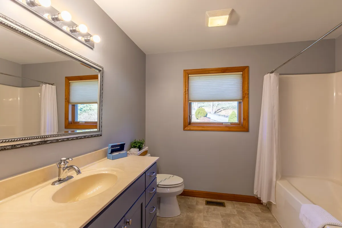 A modern bathroom with a vanity and sink, large mirror, shower curtain, and a sunlit window. The space feels fresh and clean, ideal for morning routines or relaxing baths after a day of adventure.