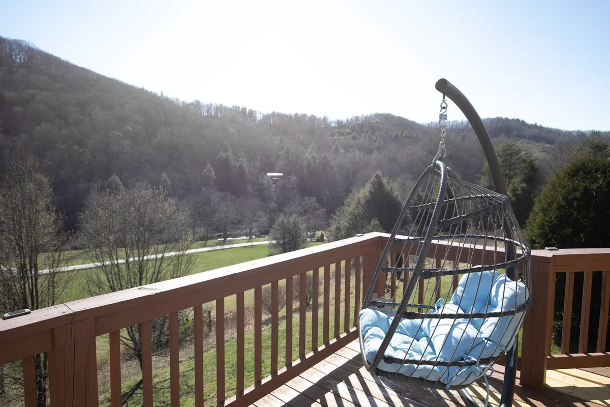 This exterior image features a hanging chair on the deck, framed by a sturdy railing and panoramic mountain views in the background. The open-air setting is tranquil, inviting relaxation and time spent outdoors, with plenty of room for you and your pet to soak in the mountain air together.